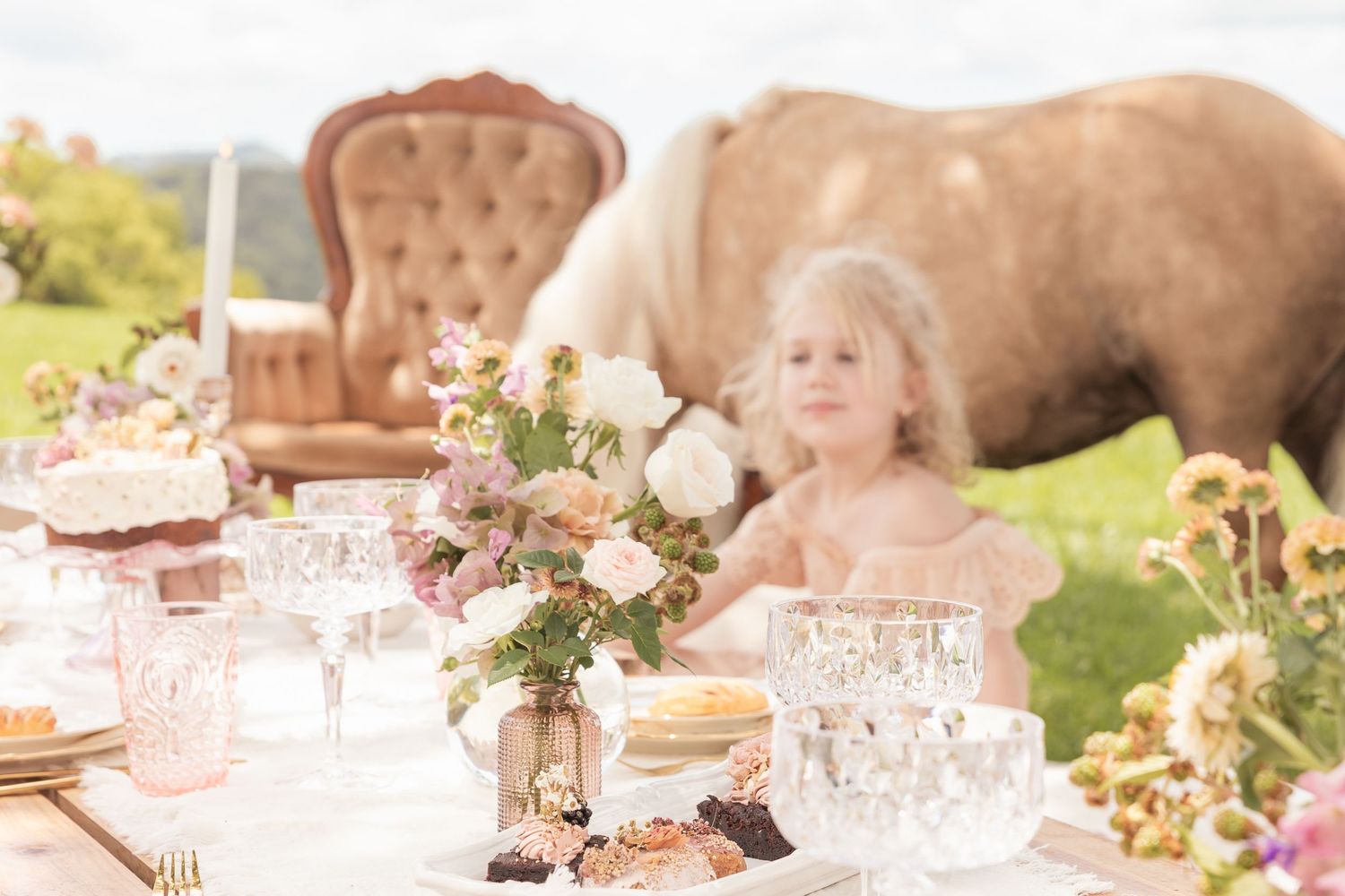 Vintage-style tea party table decorated with pink flowers and delicate glassware in an outdoor setting.