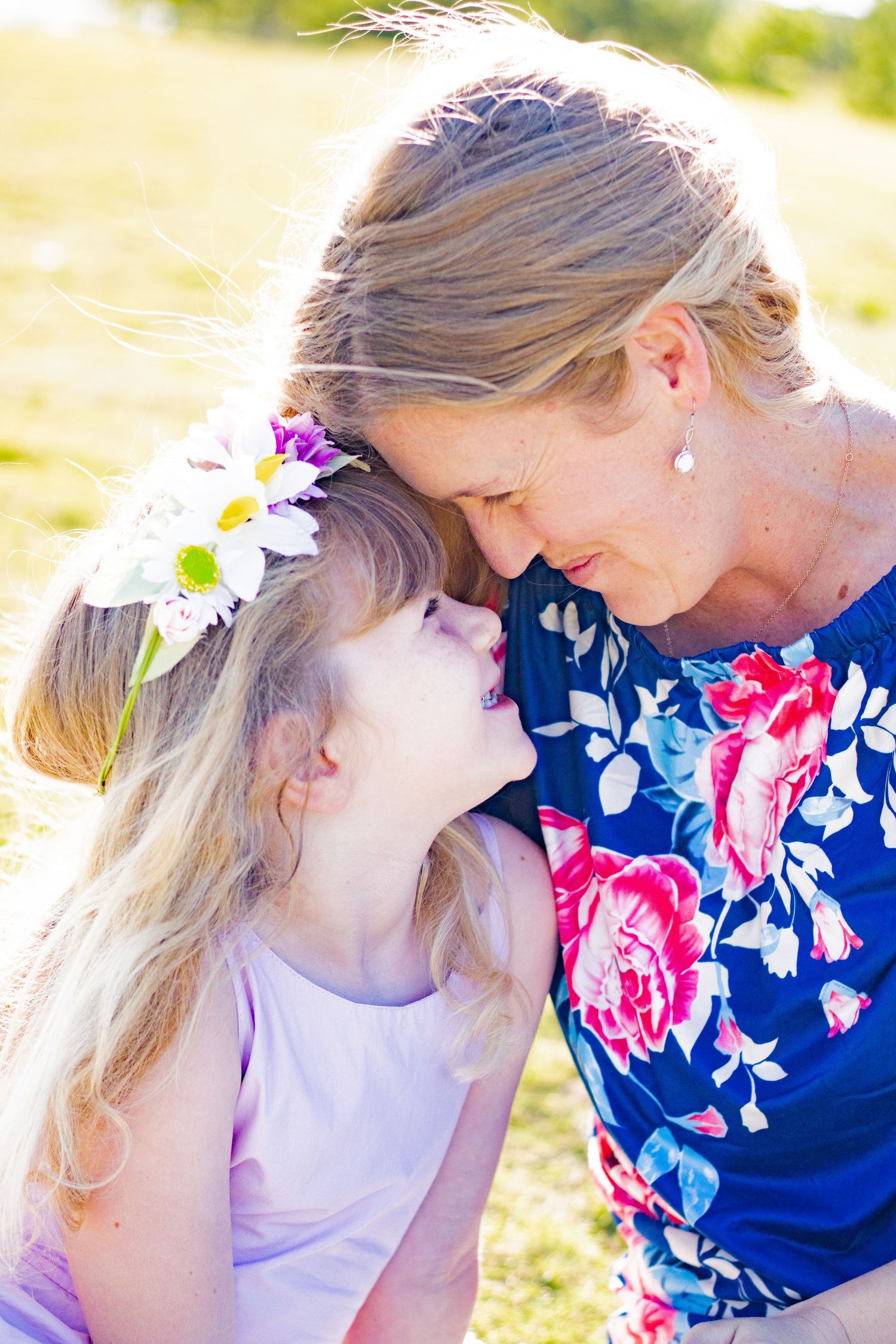 Mother and daughter share tender moments while playing outdoors in floral dress and white outfit.