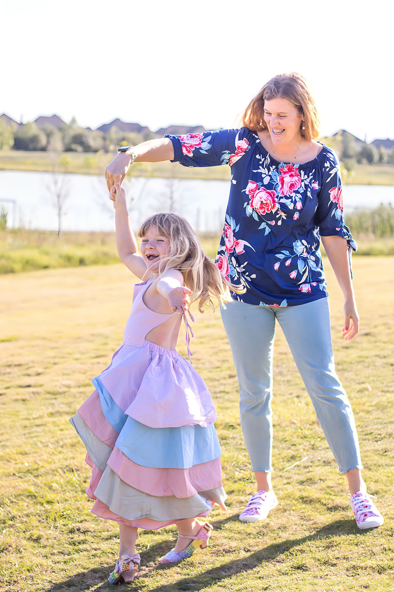 Mother and daughter twirling and playing together in a sunny field wearing coordinated blue and pink outfits.