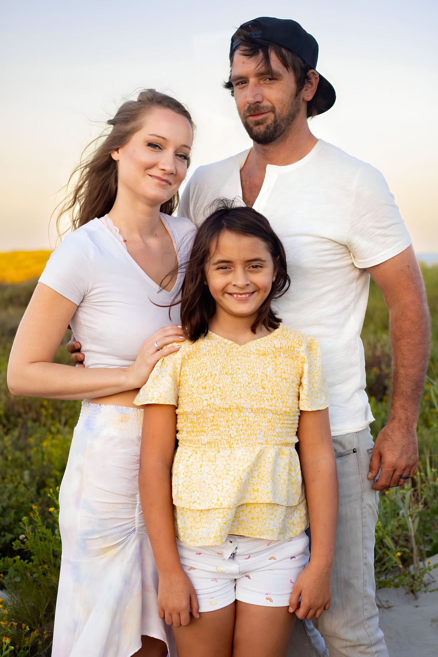 Family wearing white and yellow outfits poses together on beach during sunset.