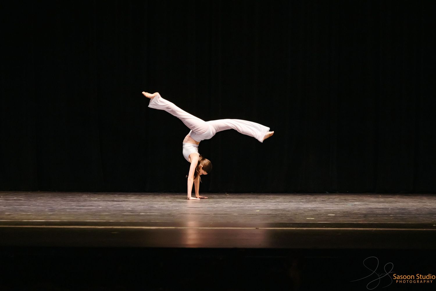 A dancer performs a graceful handstand on stage in dramatic lighting.