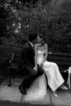 A black and white photo series shows a couple sitting on a park bench in wedding attire with playful poses.