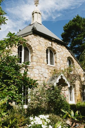Charming stone chapel with arched windows and ornate spire nestled among garden foliage.Best wedding photographer in Adelaide SA