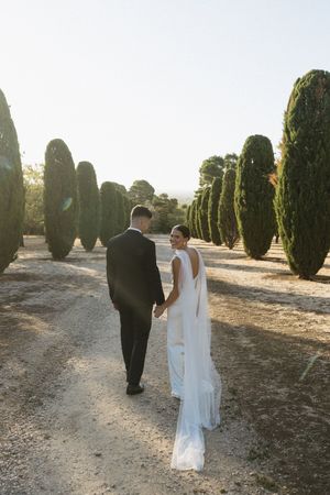 Couple walking hand in hand down path lined with tall cypress trees during sunset wedding photo session. Best wedding photographer