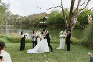 Intimate lakeside wedding ceremony with floral arrangements and guests on grassy shore. Best wedding photographer in Adelaide SA
