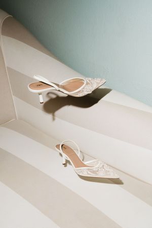Two white lace pointed-toe slingback kitten heels displayed on striped steps with soft natural lighting.