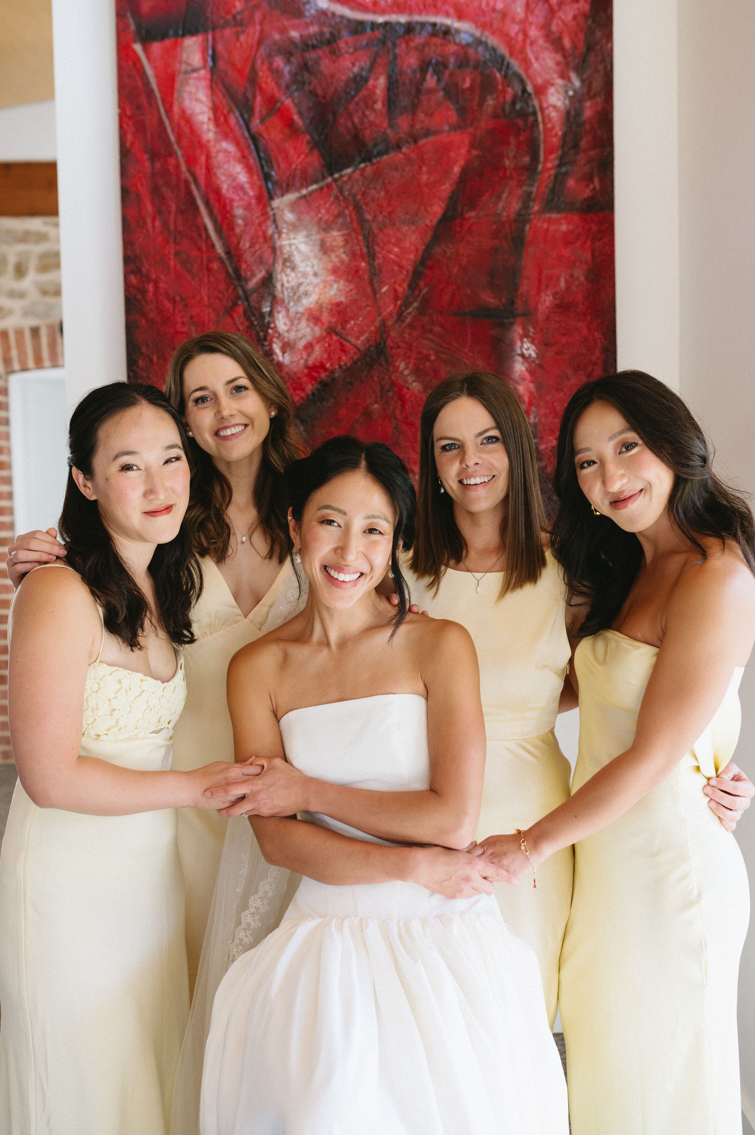 Bridesmaids in pale yellow dresses pose together against a dramatic red art backdrop. Best wedding photographer in Adelaide SA