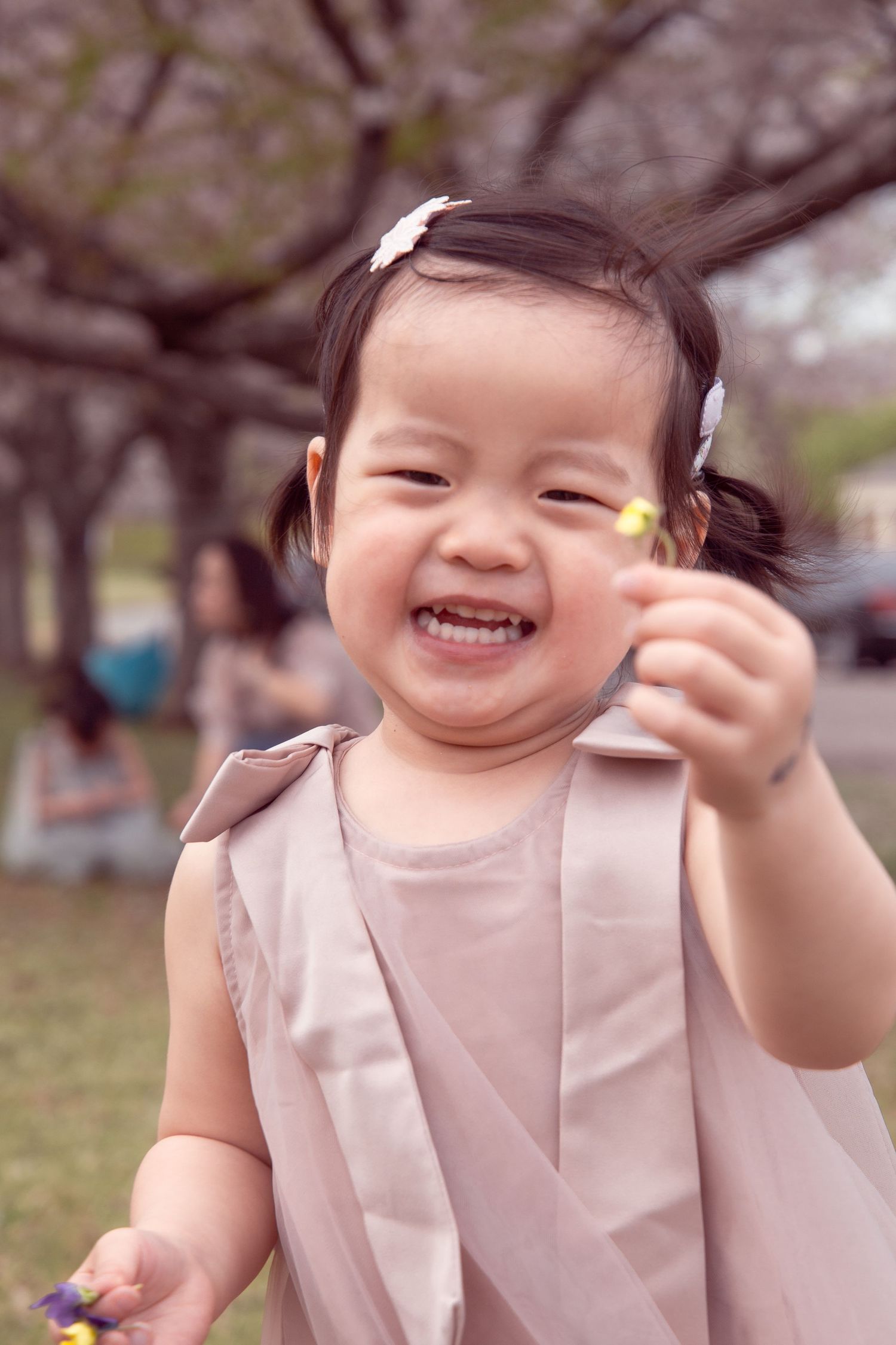 Young child in beige dress smiling and playing outdoors during spring.