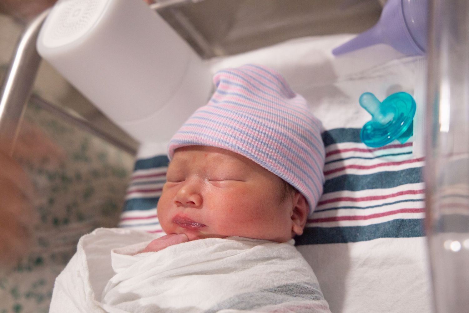 Newborn baby sleeping peacefully in hospital bassinet wearing striped hat.
