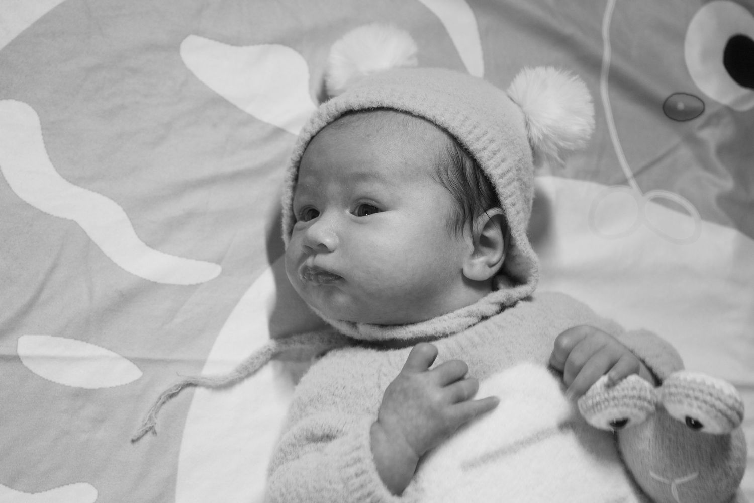Newborn baby wearing soft knit hat rests on white blanket.