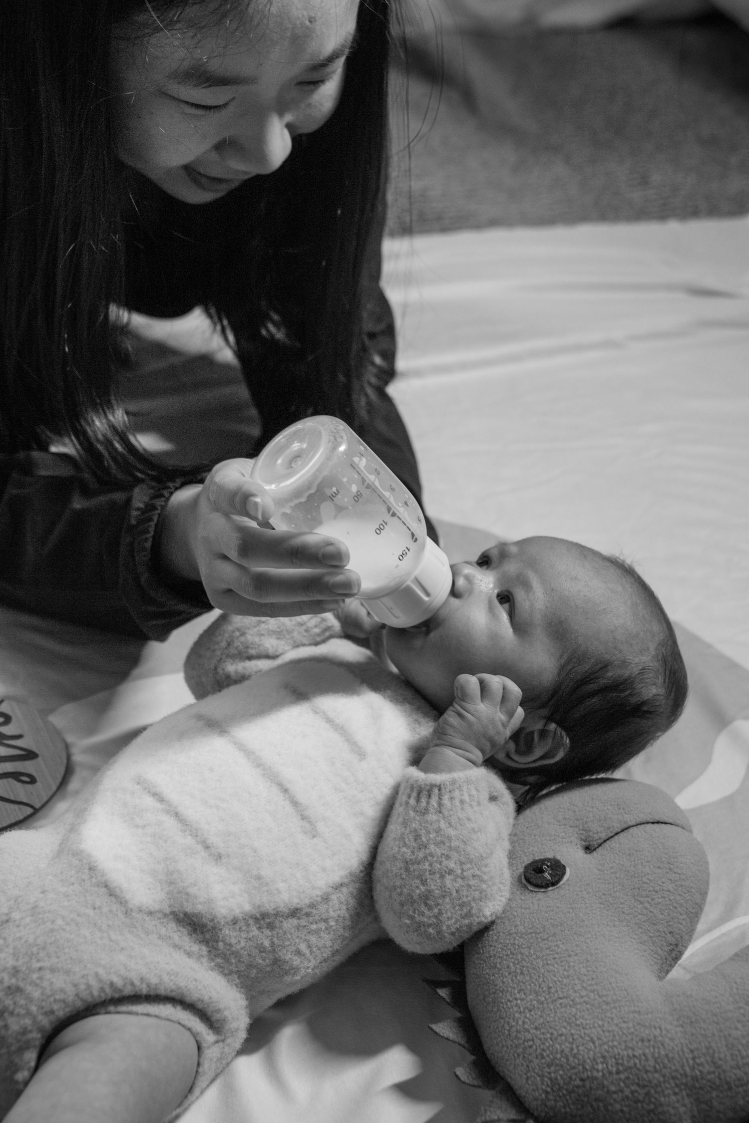 Caregiver bottle feeding infant on soft white blanket in black and white.