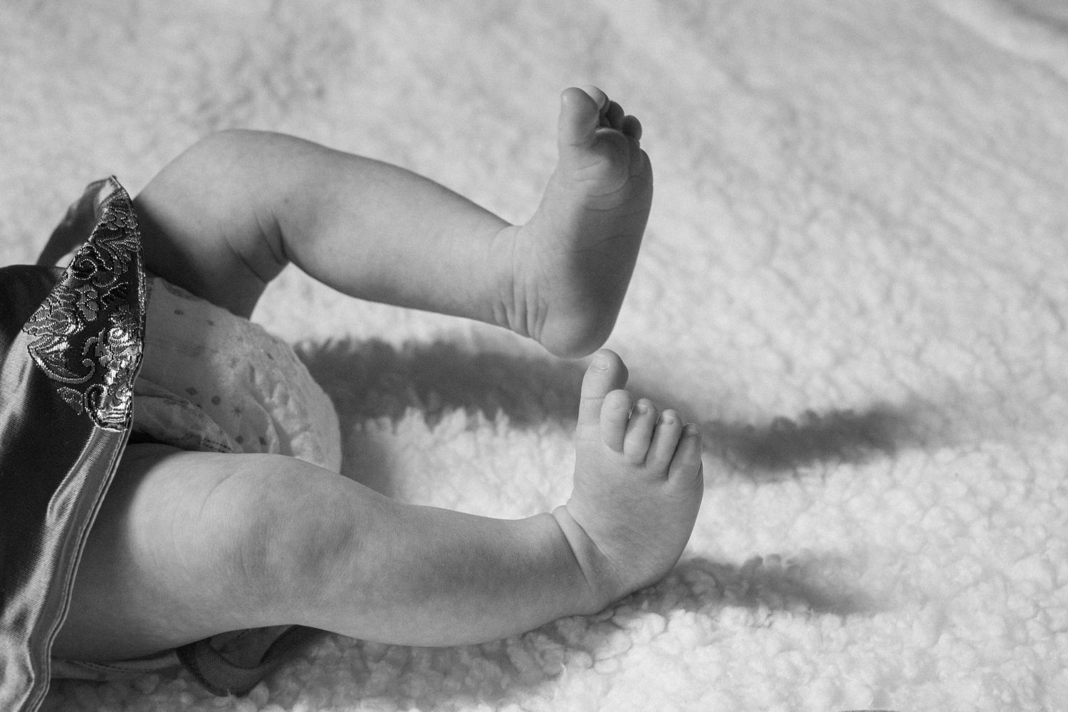 Black and white image of tiny baby feet and legs on white fabric.