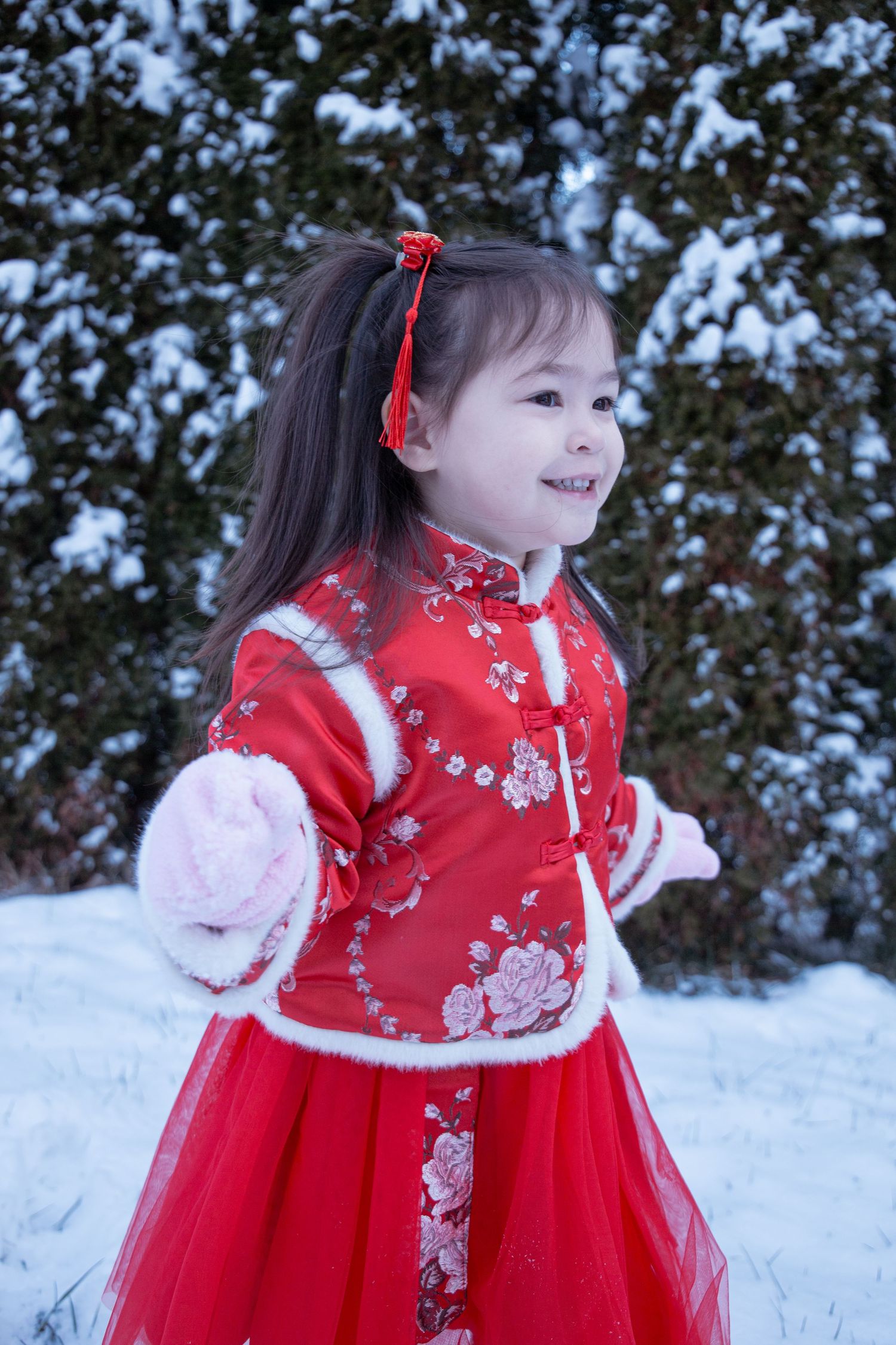 Child in festive red Chinese dress twirling in the snow.