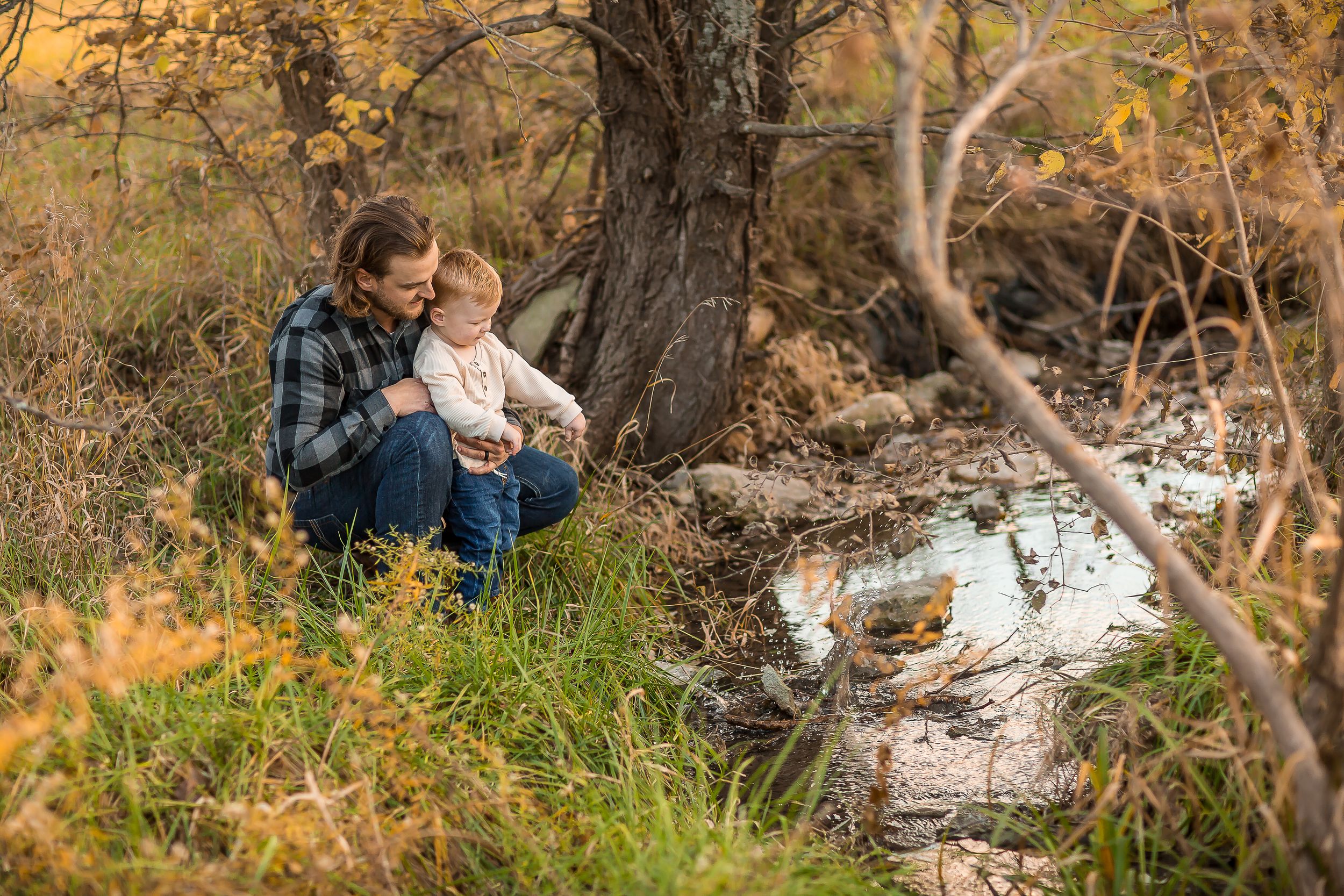 Mother and child sitting together by a small stream in an autumn forest with golden foliage.