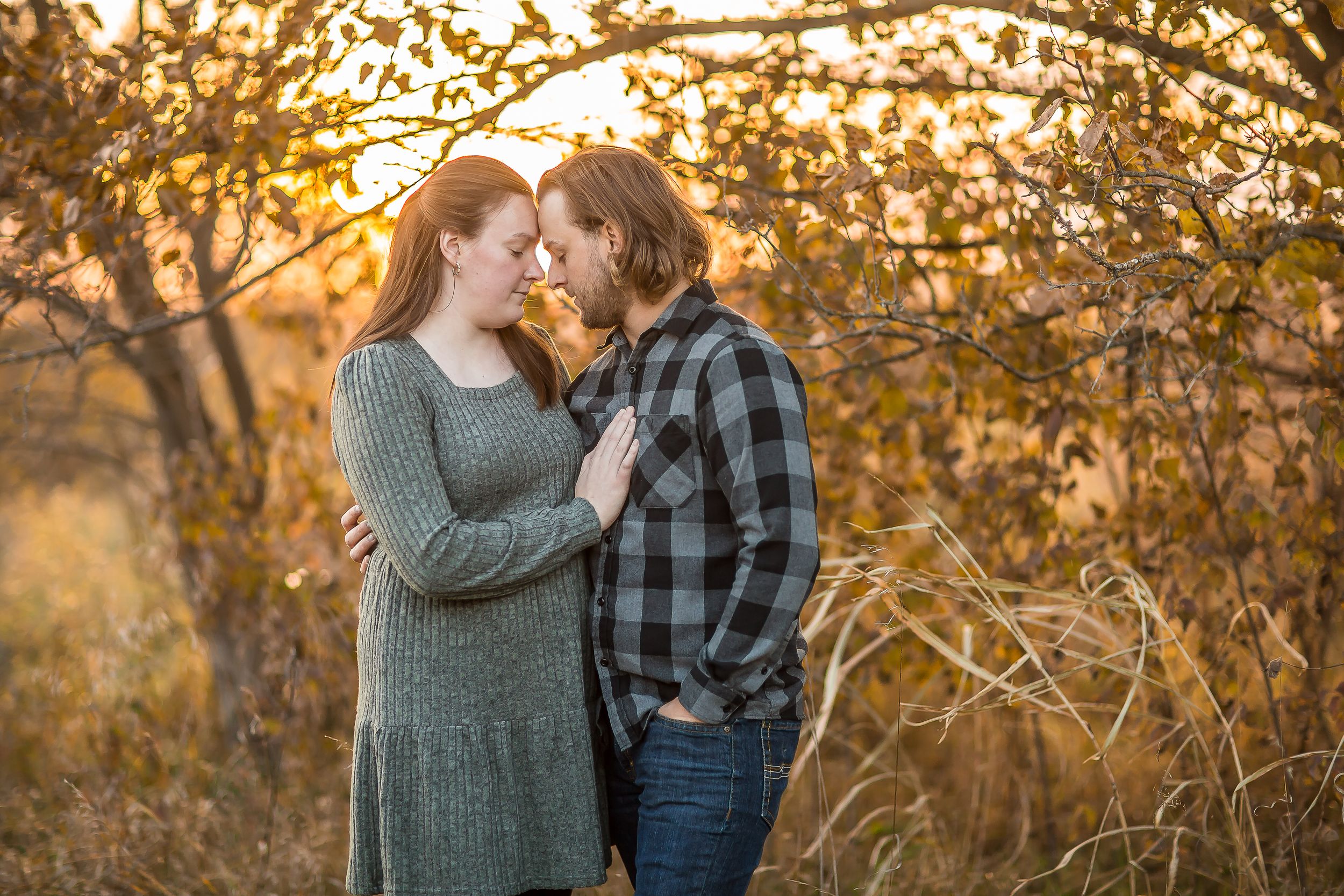 Couple sharing a romantic moment outdoors at golden hour, surrounded by autumn foliage and warm sunlight.