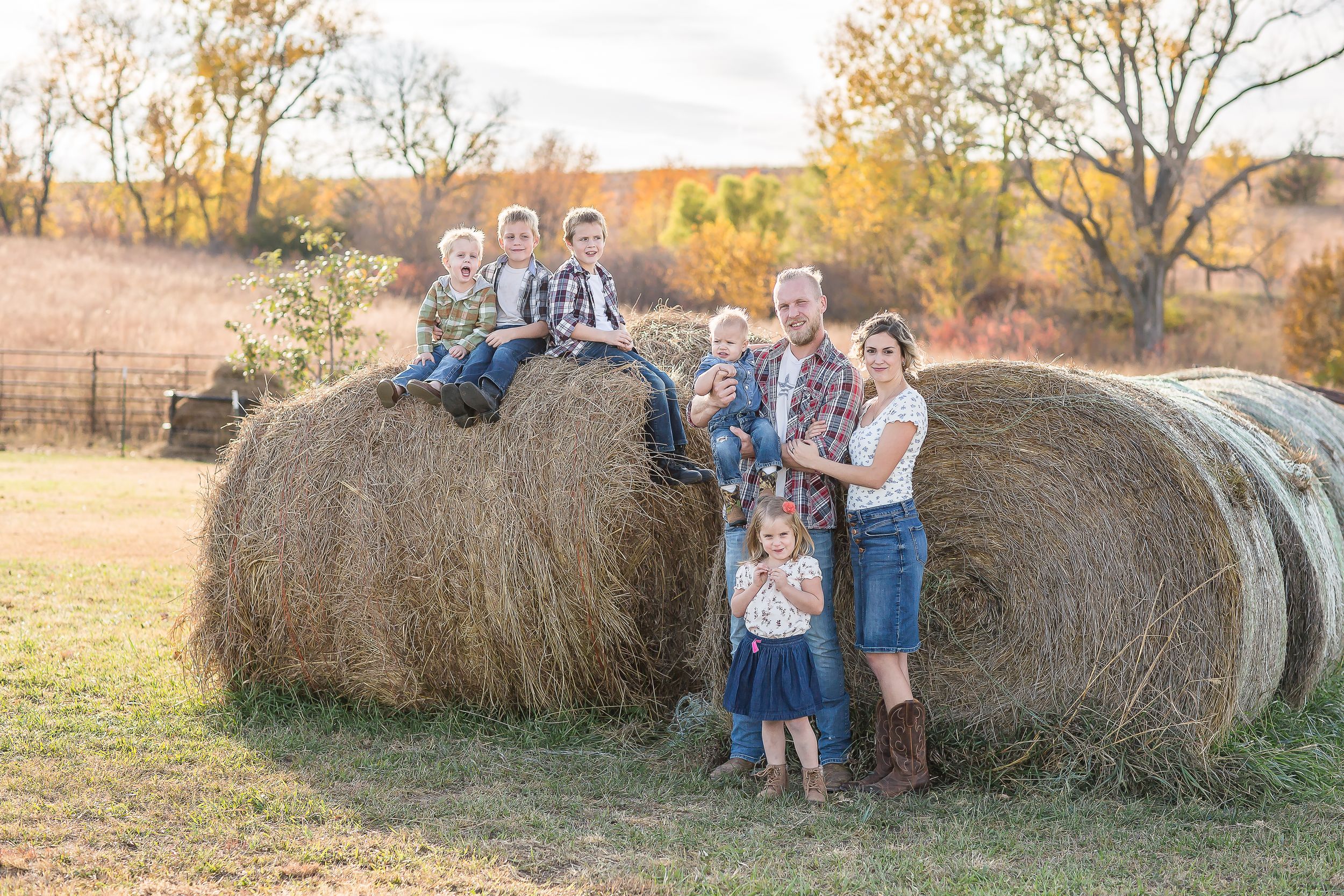 Family posing with large hay bales in an autumn field during a fall outdoor photo session.