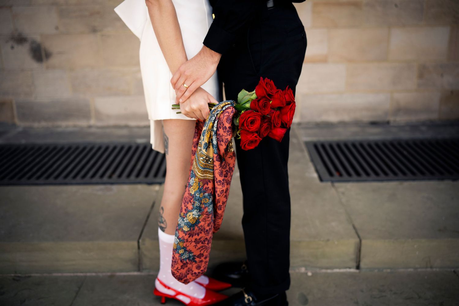 Romantic close-up of a couple holding hands, with red roses and vintage fashion—capturing love, style, and heartfelt moments.
