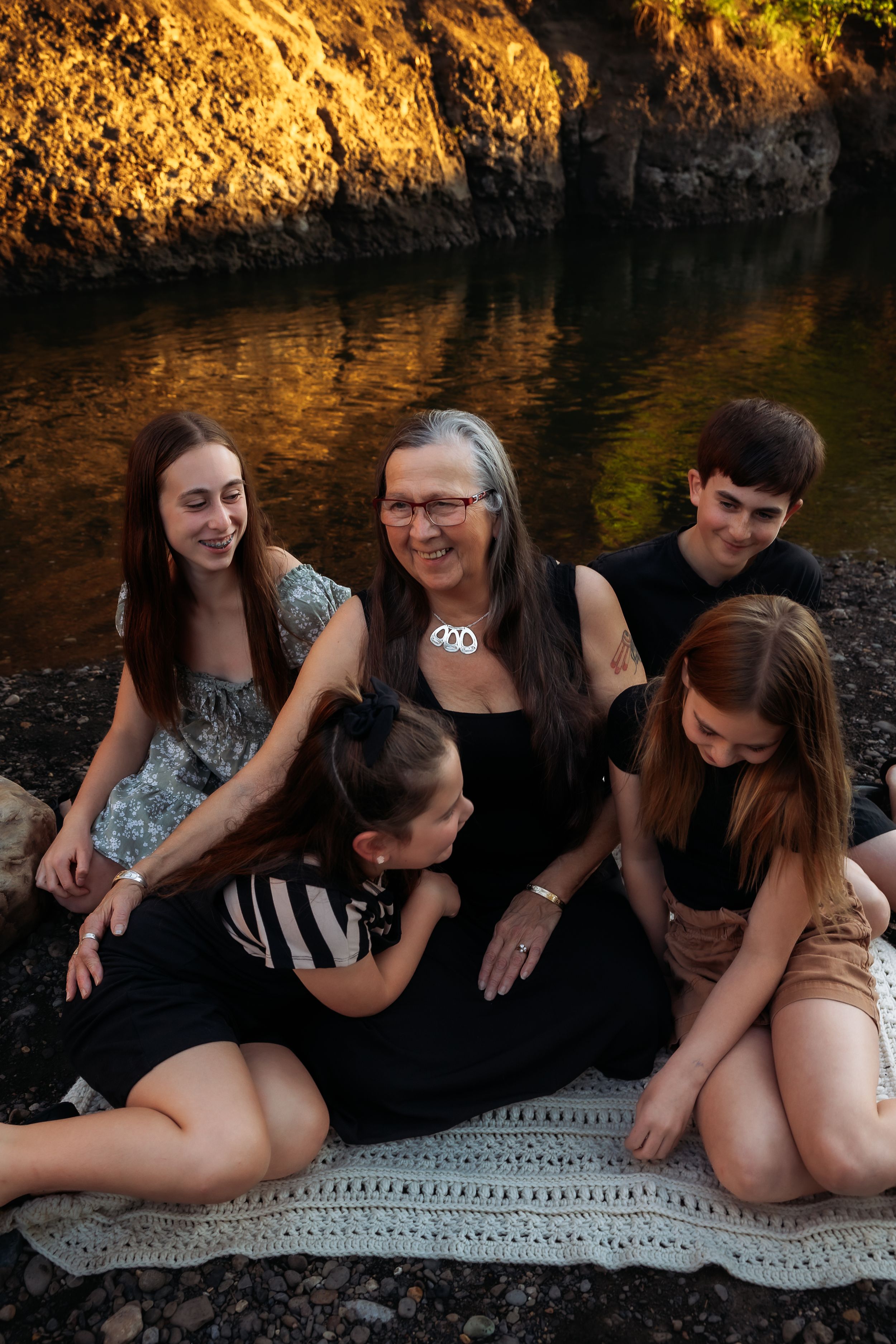 A group sits together on a white blanket against a stone wall during a warm sunset photoshoot.