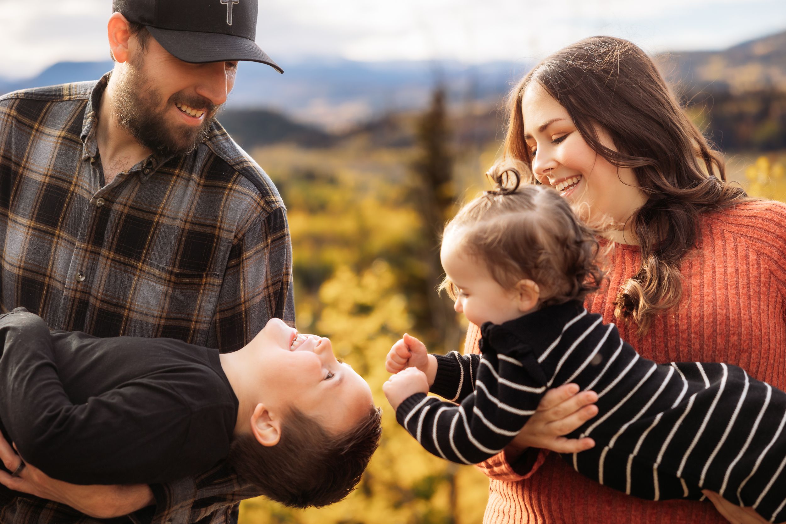A couple embraces and laughs together during a golden hour photoshoot in a scenic mountain landscape.