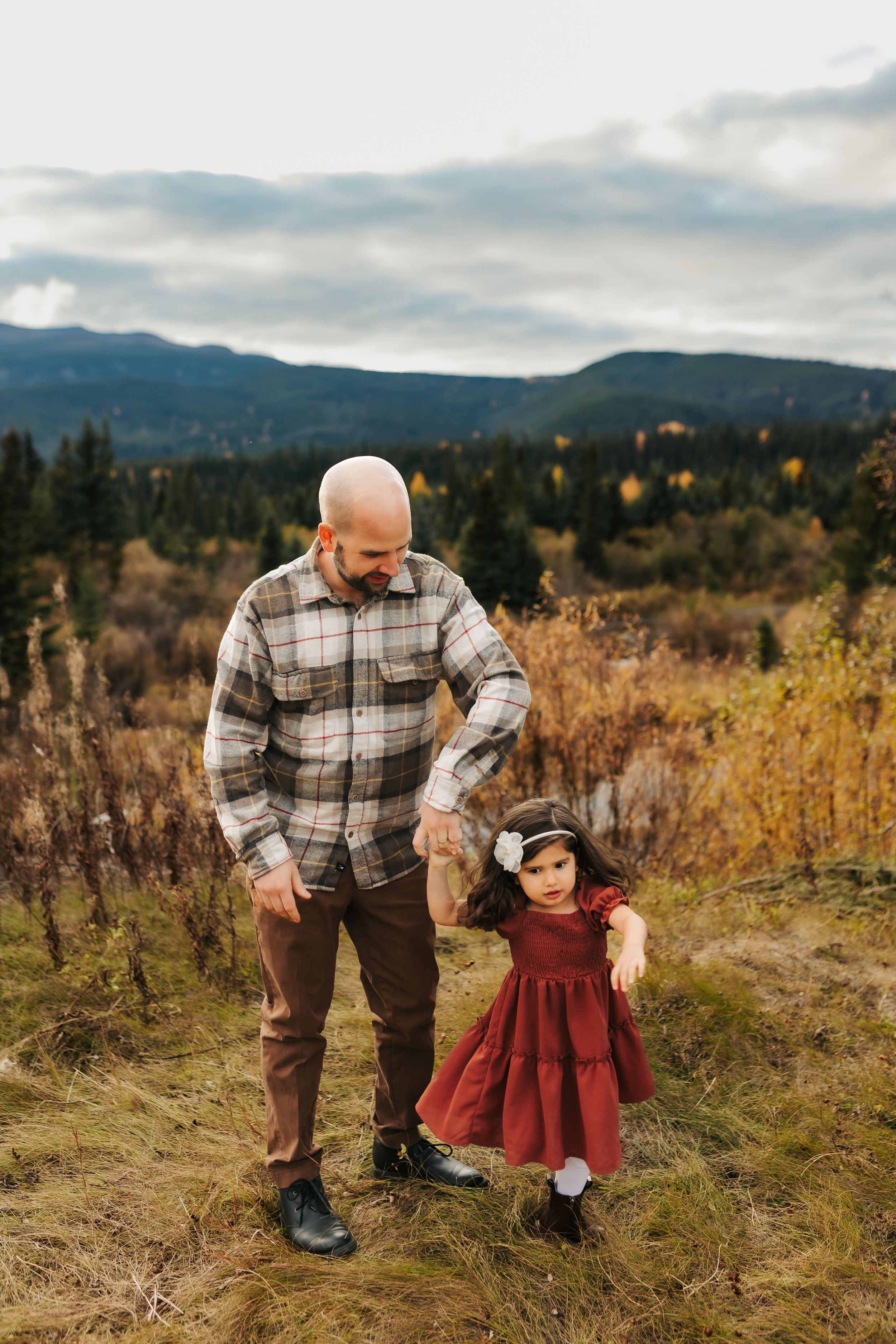 Adult and child in matching plaid and red outfits pose on mountain trail.