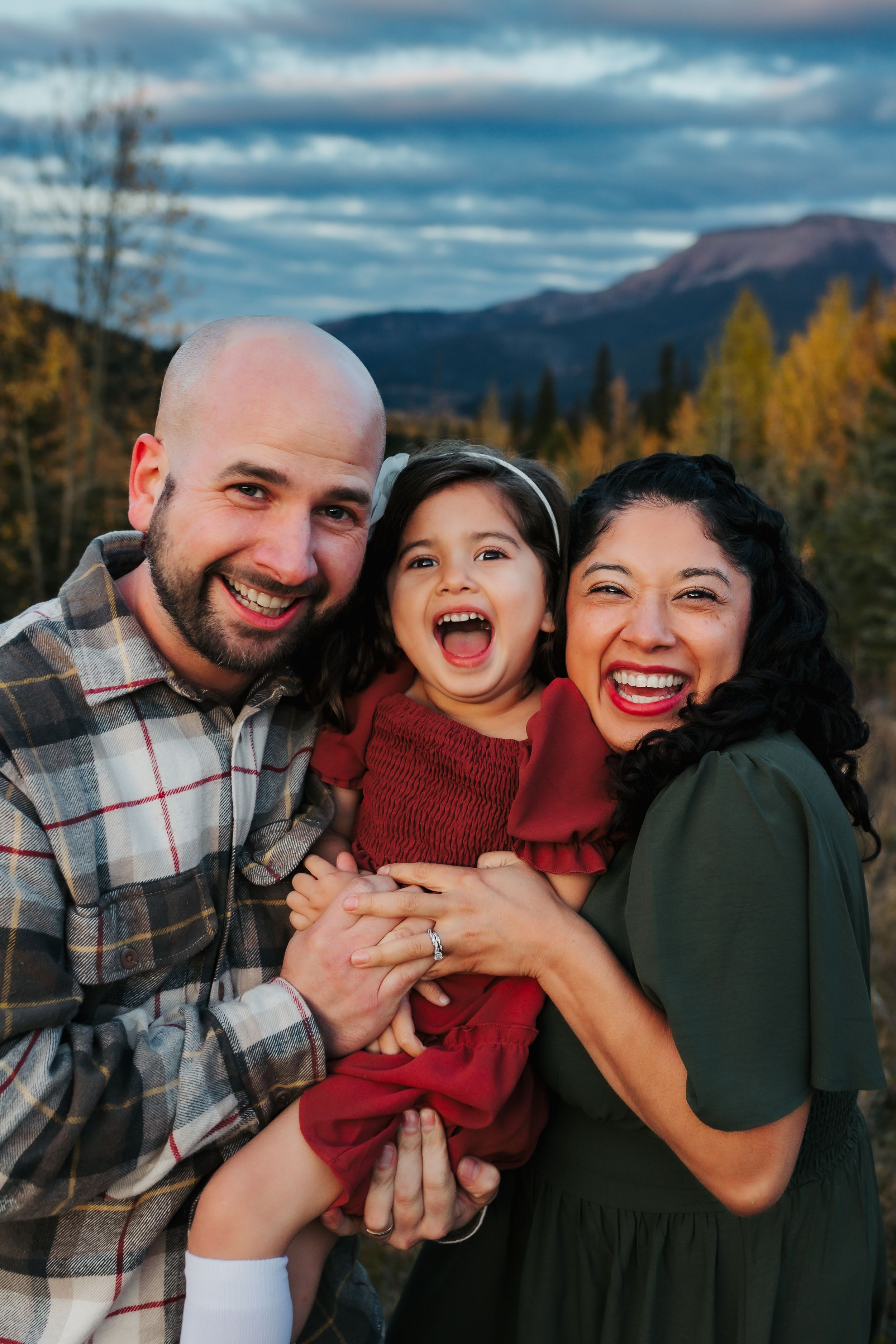 A happy family portrait outdoors with mountains and autumn colors in the background.