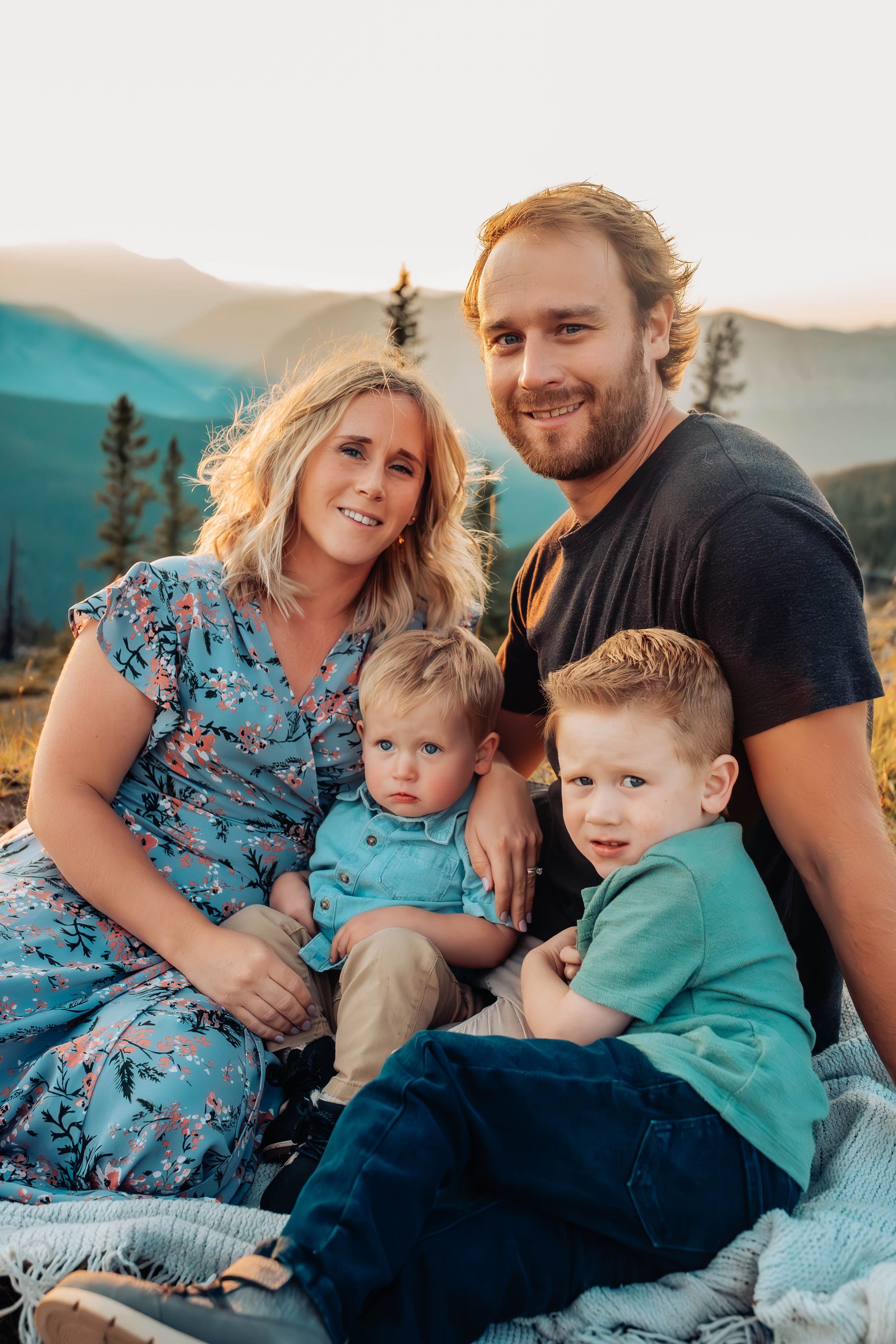 Family cuddles together on mountain overlook during sunset photoshoot.