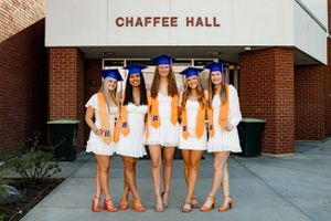 five grads posed together in front of a dorm building