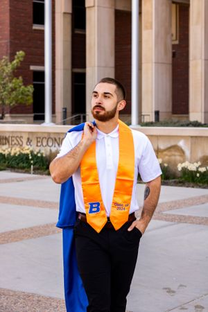 a grad walking towards the camera with his gown of his shoulder