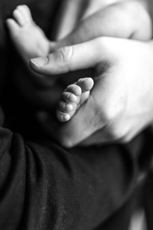 Artistic black and white macro photography of baby fingers and hands against dark background.