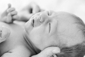 Black and white portrait of sleeping newborn baby on soft white bedding.