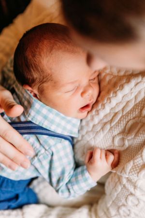 Newborn baby wearing blue checkered outfit resting on textured white blanket.