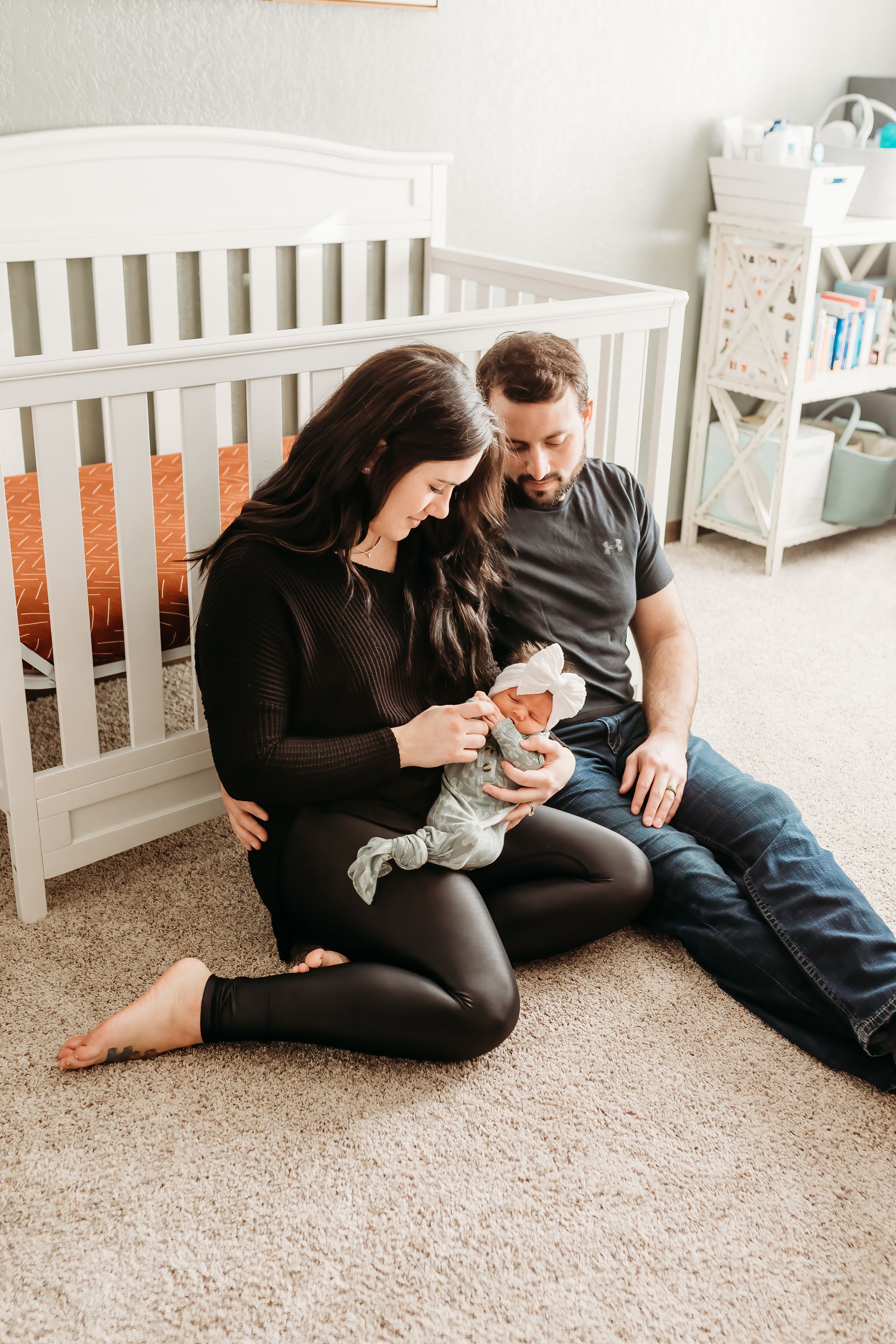 Family lifestyle session with newborn baby on carpeted floor near white crib.
