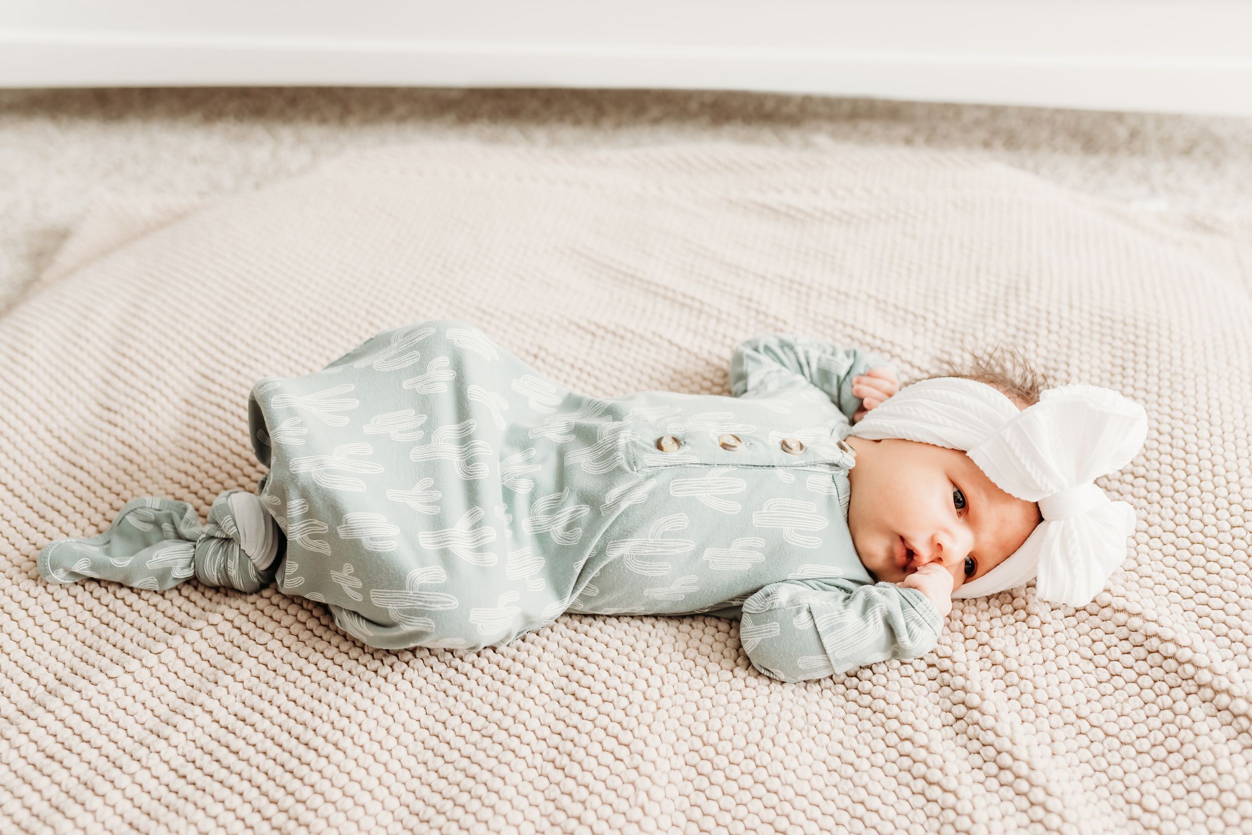 Newborn baby lying on soft beige blanket in natural light.