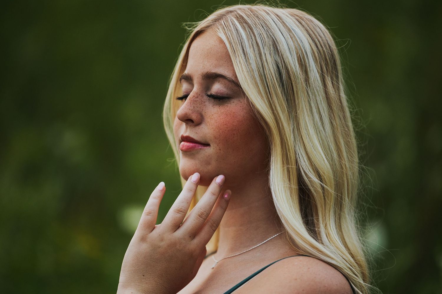 An artistic portrait showing someone with light hair against a dark green natural background.