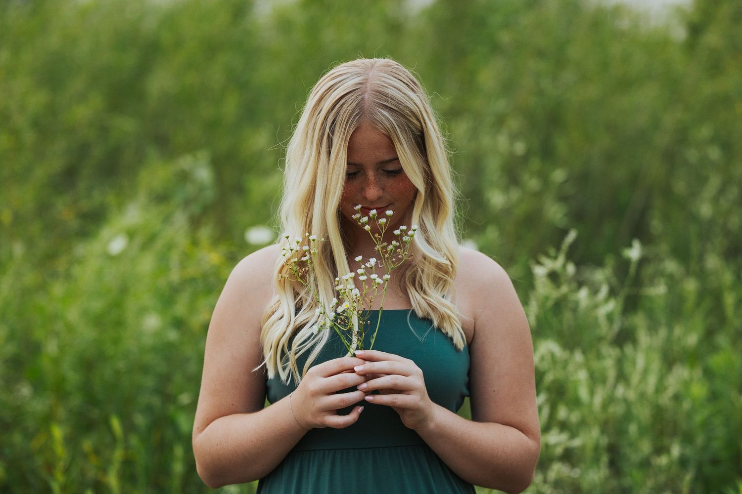 A serene portrait of someone in a teal dress holding dried flowers in a natural outdoor setting.