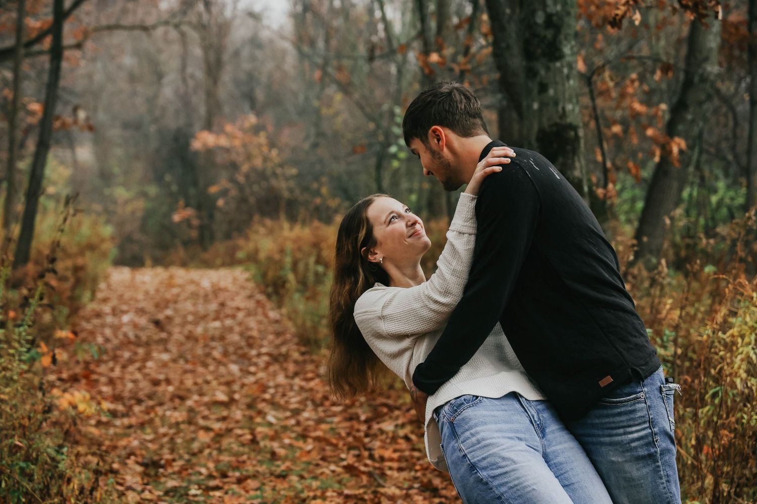 A couple shares a romantic dance pose amongst fallen autumn leaves in the woods.