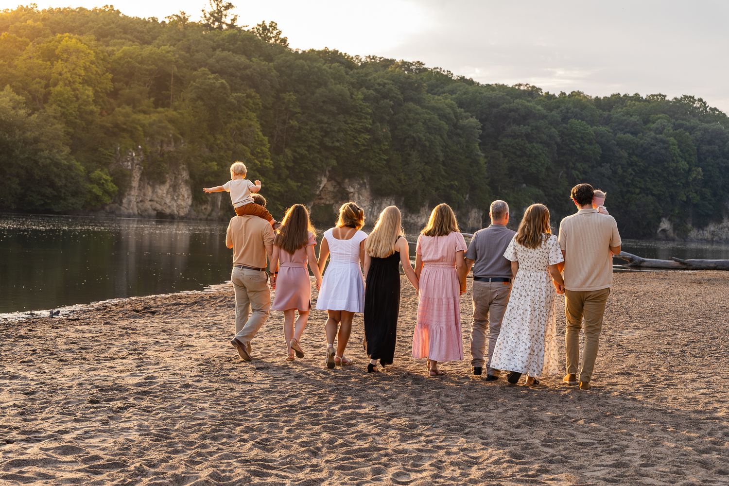 A group of people walking together on a sandy beach at sunset beside a lake with cliffs in the background.