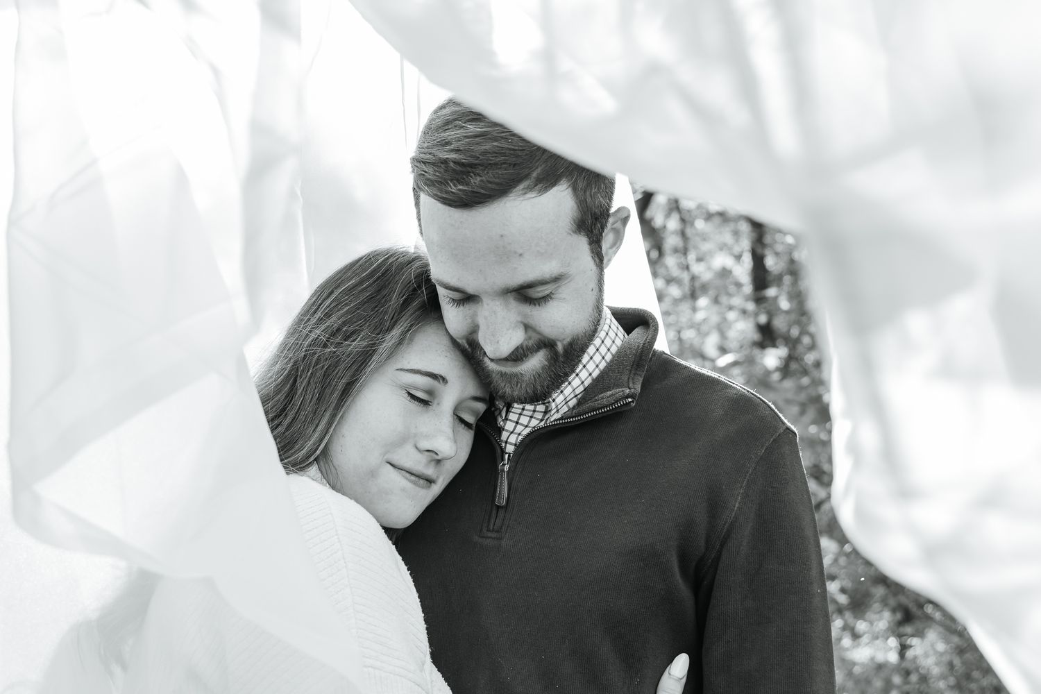 Black and white romantic couple portrait showing intimate embrace against blurred background.