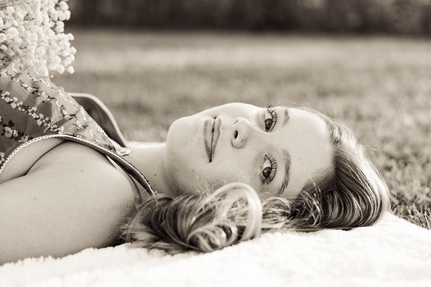 A black and white portrait of someone lying on their side in grass with a serene expression.