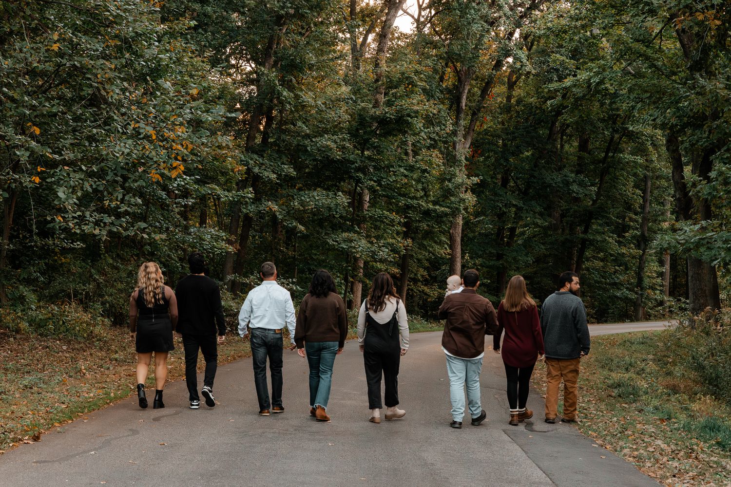 A group of people walking together on a leaf-covered path through an autumn forest.
