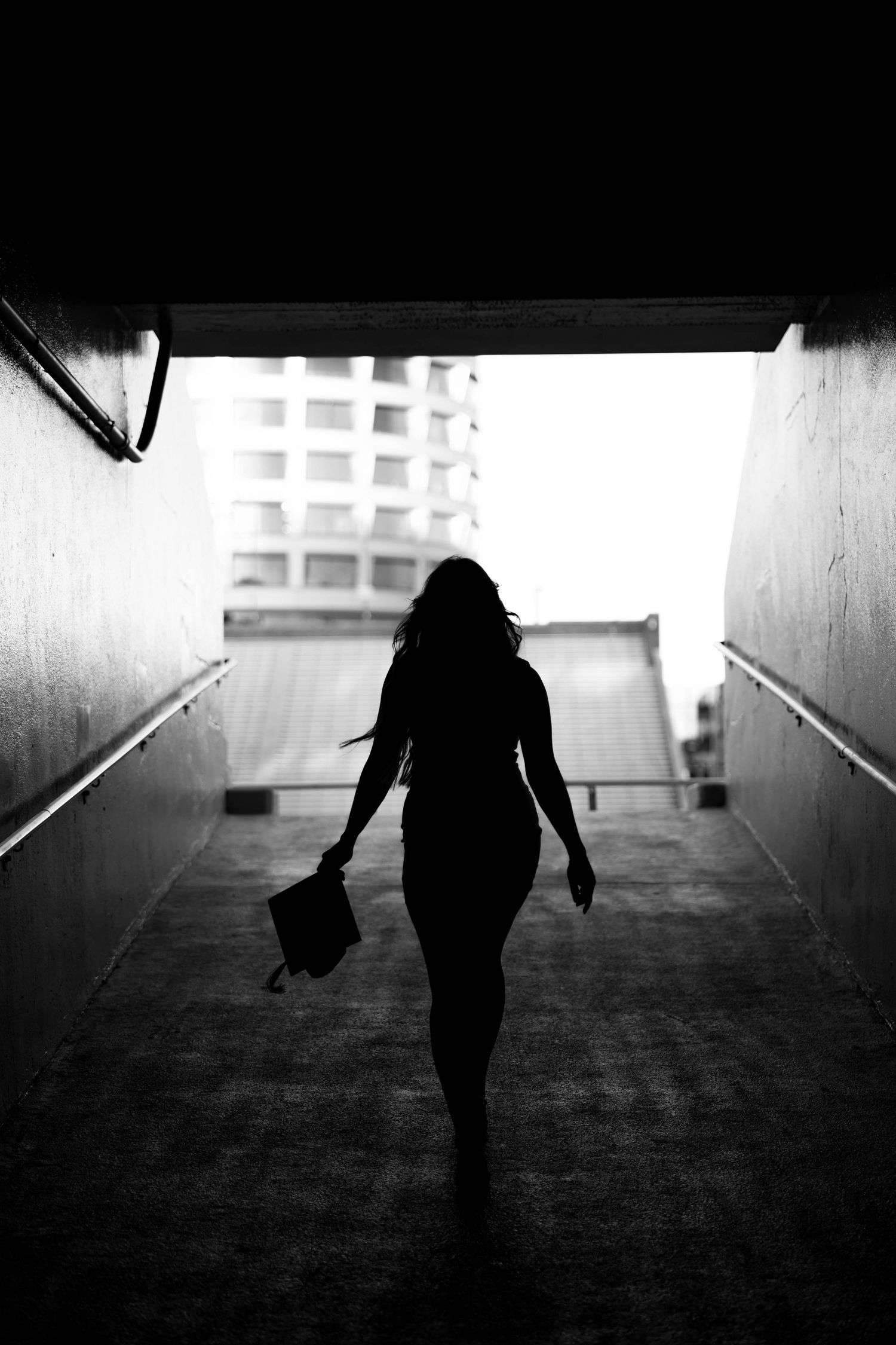 Silhouette of a person walking through a tunnel with a bag while holding their hand outward against a bright exit.