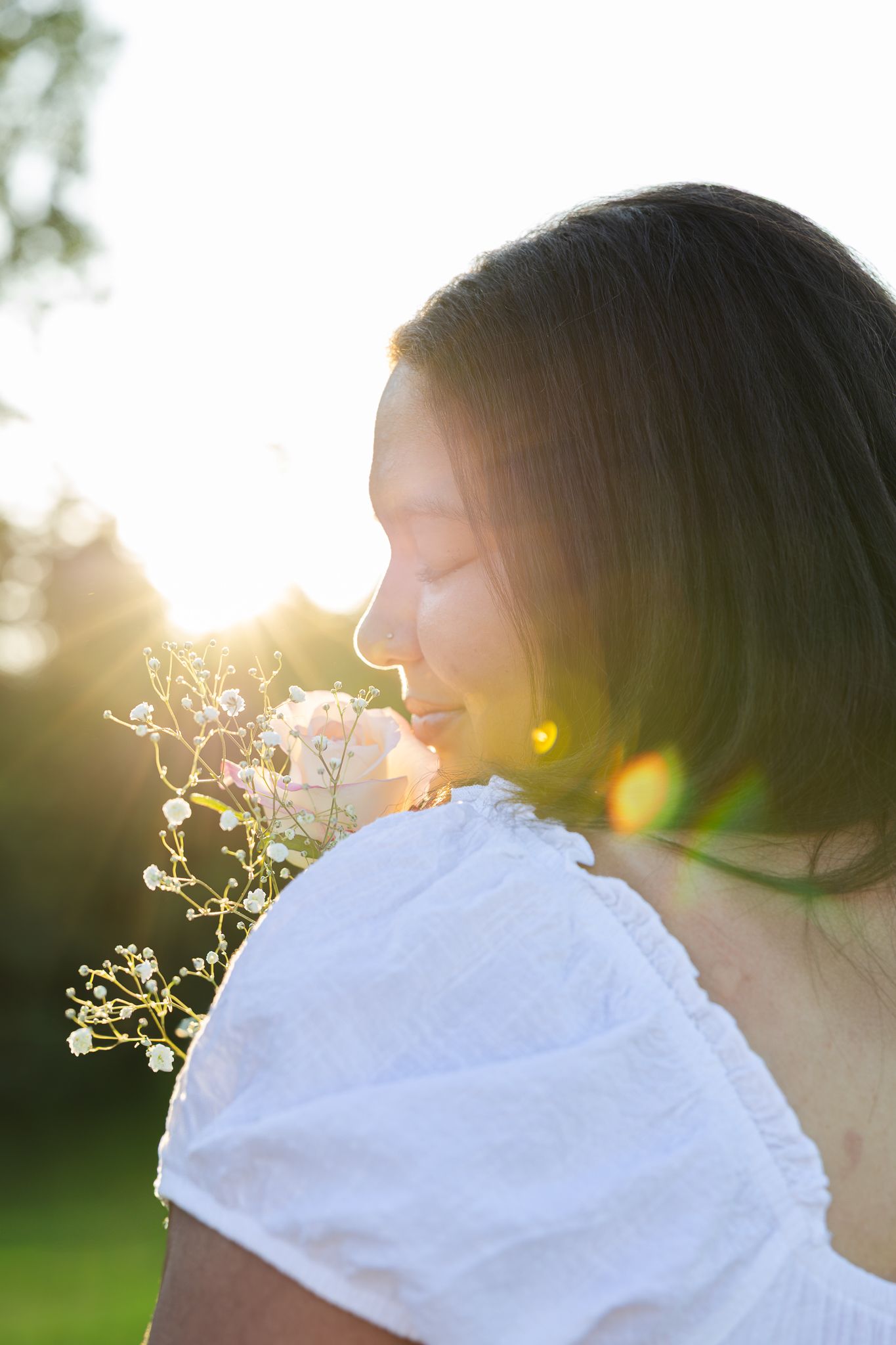 Silhouette of person in white dress holding delicate flowers against golden sunlight in garden setting at sunset.