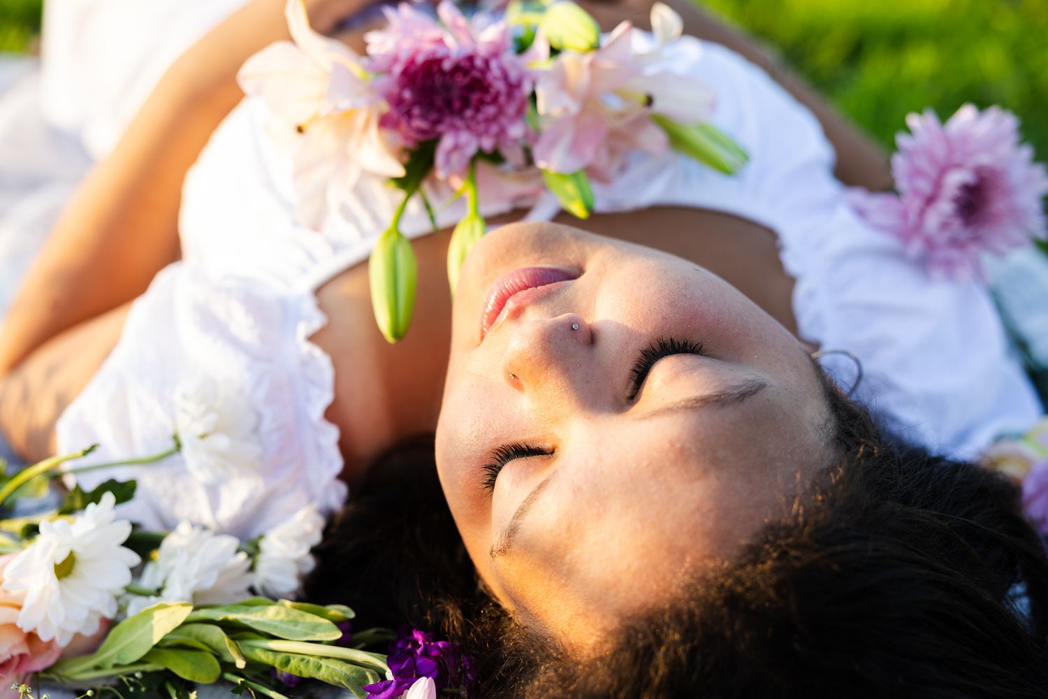 Someone laying in grass surrounded by purple and white flowers on a sunny day.