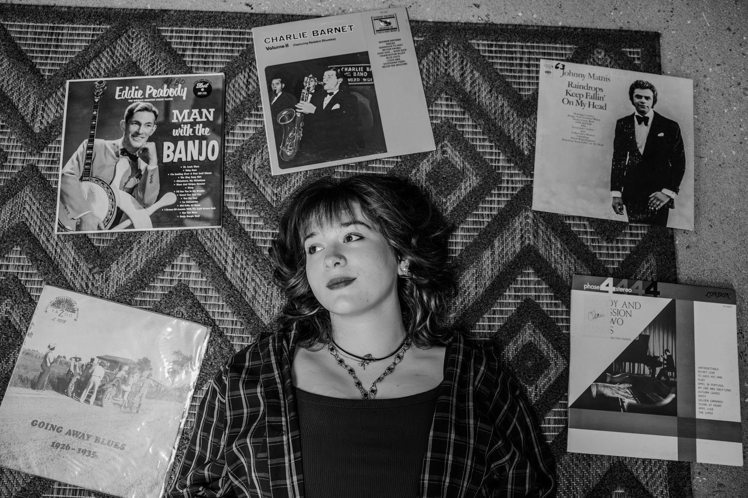 Black and white photo of a bedroom wall decorated with vintage album covers and music posters.