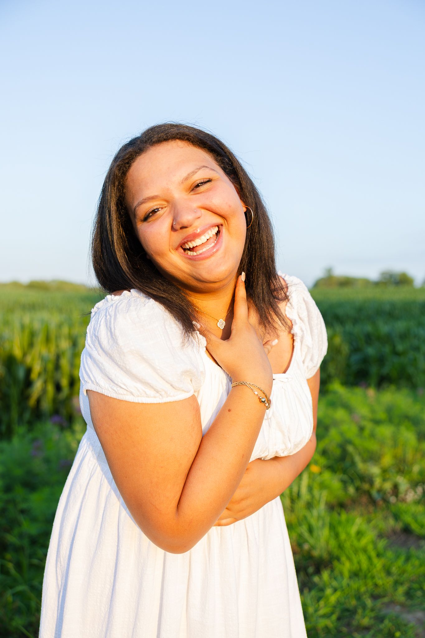 A person in a white dress laughs joyfully in a series of candid shots taken in a lush green field.