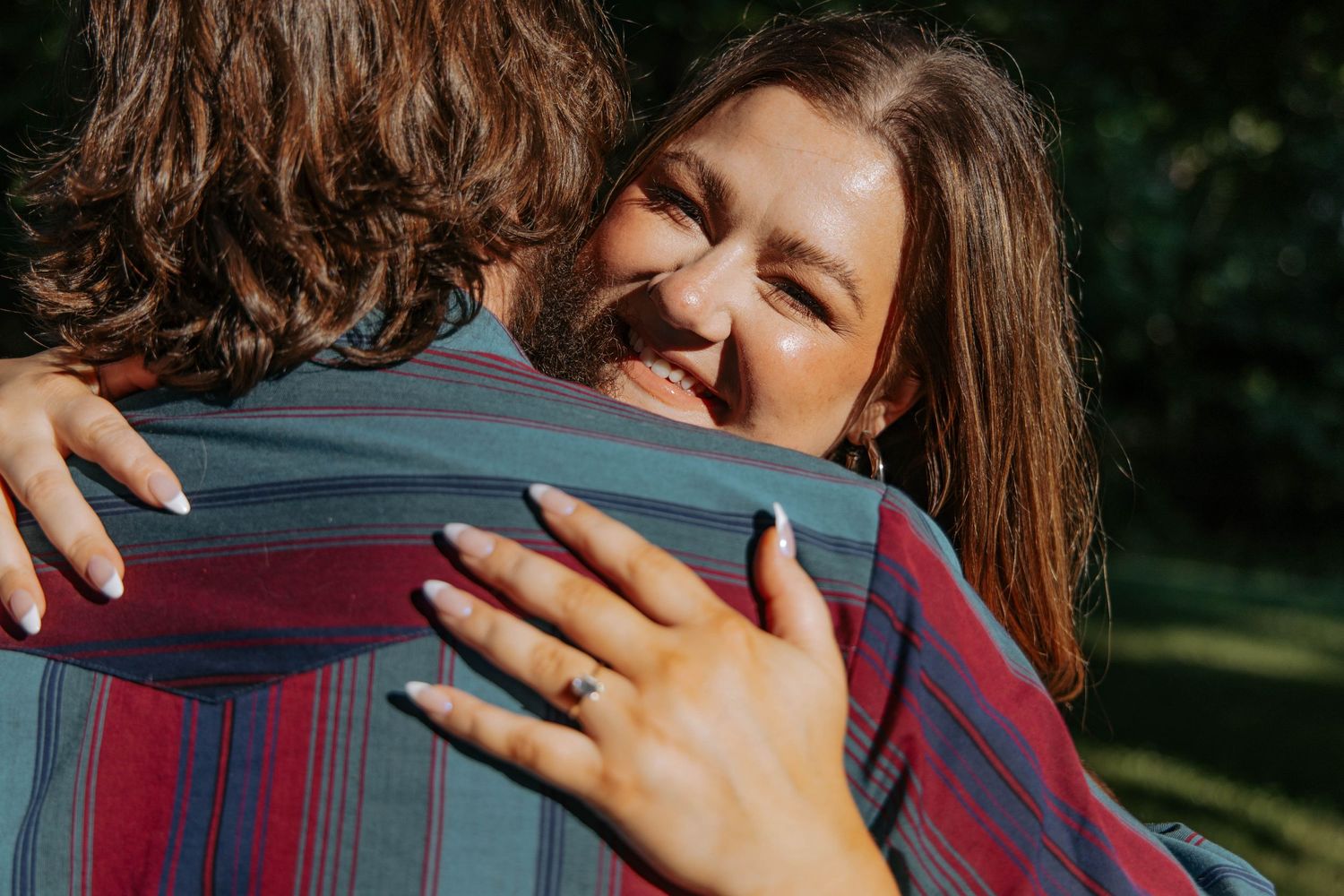 Two people sharing a warm embrace outdoors on a sunny afternoon.