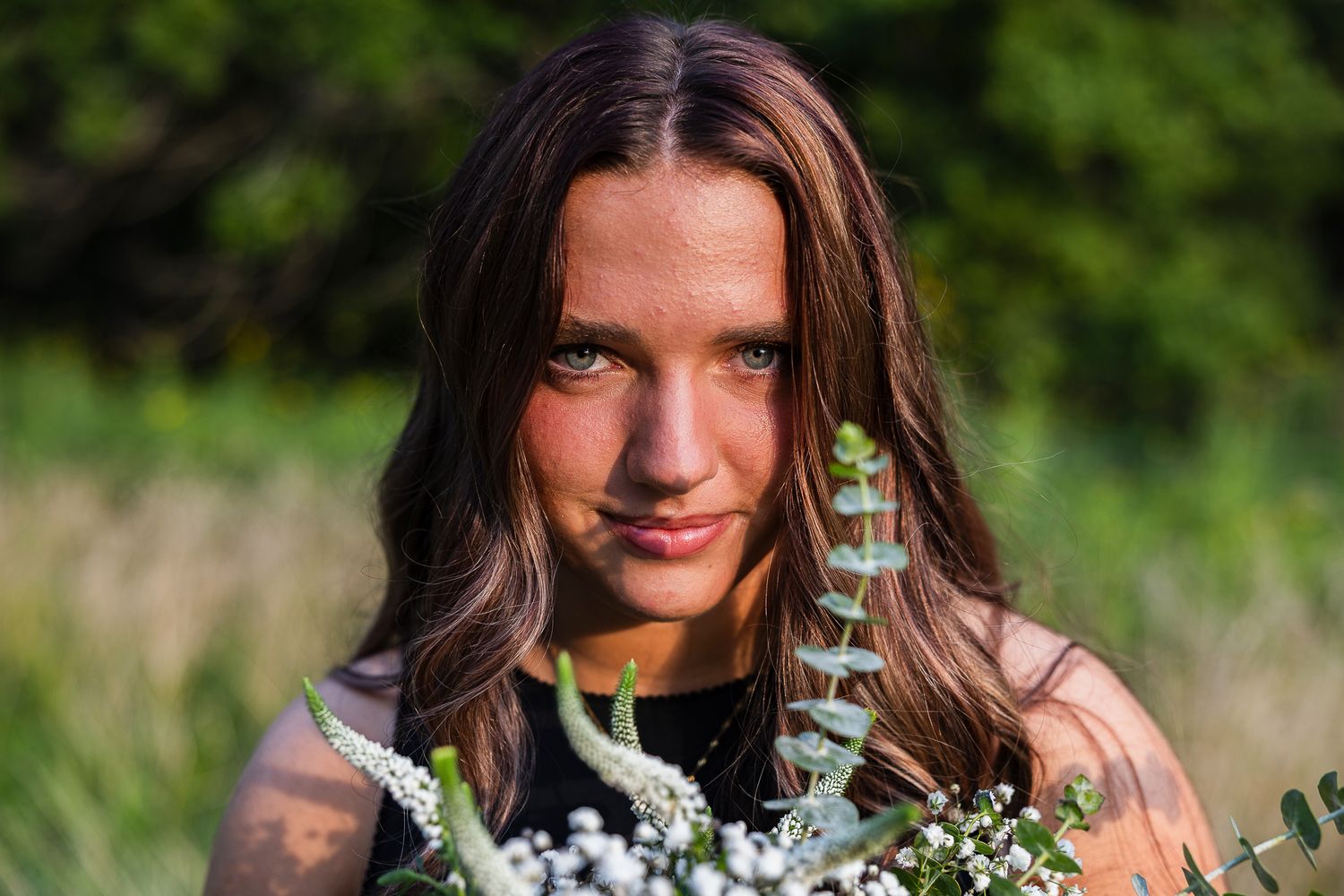 A person holding a wildflower bouquet stands in a sunny meadow on a bright summer day.