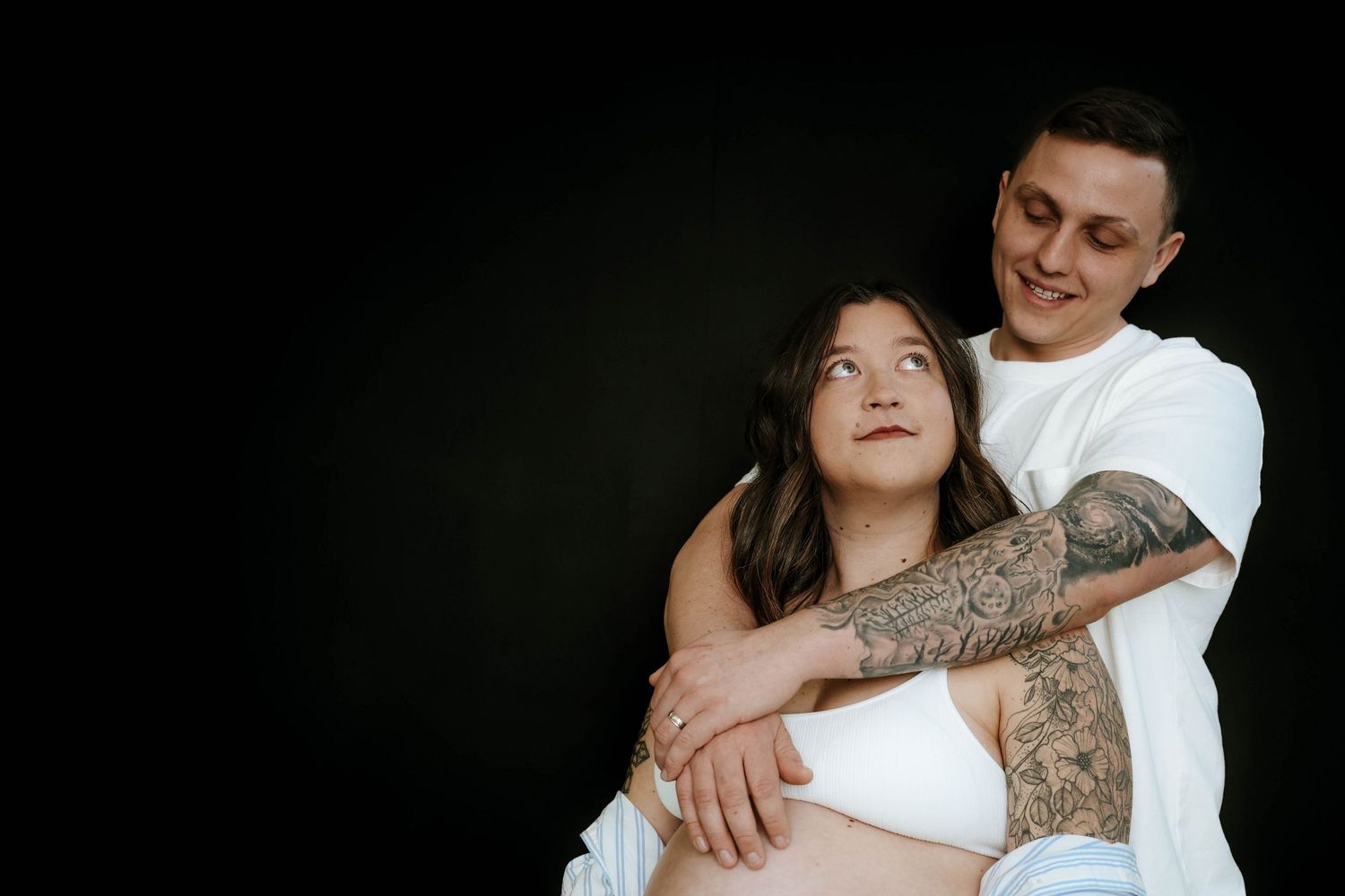 Intimate maternity photo, couple embraces on black background with loving emotion showing in black and white.