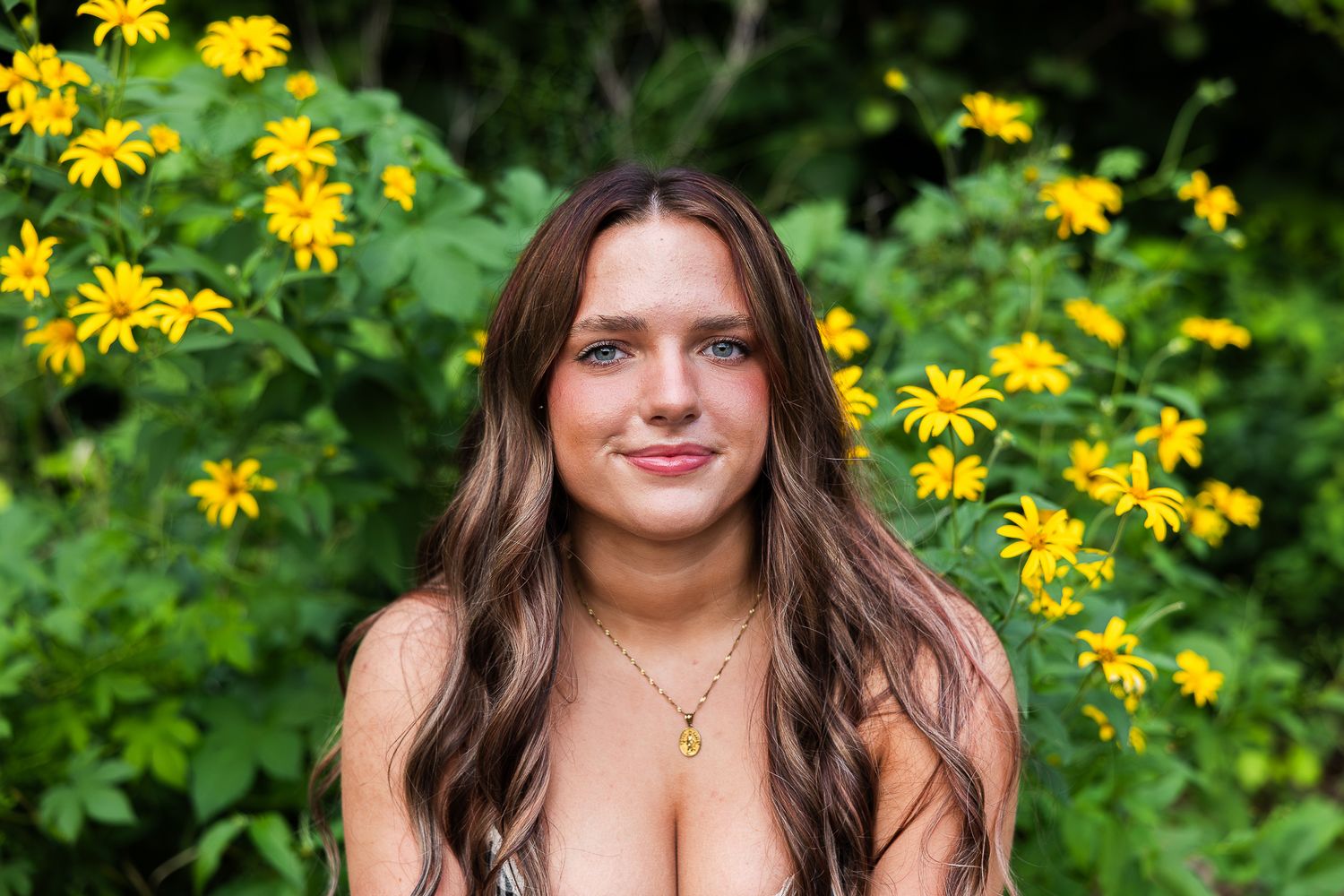 A person poses in a garden with bright yellow flowers and lush green foliage in the background.
