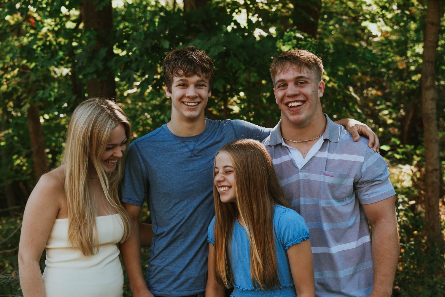 Group of four friends smiling together outdoors in casual attire.
